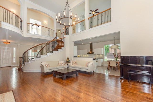 living area with a high ceiling, ceiling fan with notable chandelier, stairs, wood finished floors, and visible vents