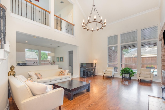 living room with crown molding, a high ceiling, wood finished floors, and a chandelier