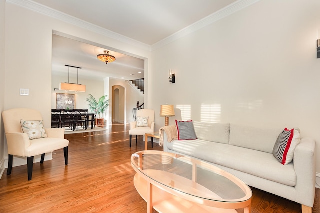 living room featuring crown molding, arched walkways, and light wood-style flooring