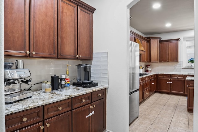 kitchen with decorative backsplash, light stone counters, arched walkways, appliances with stainless steel finishes, and light tile patterned floors