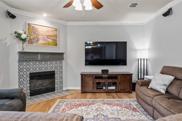 living area with visible vents, ornamental molding, wood finished floors, a fireplace, and ceiling fan