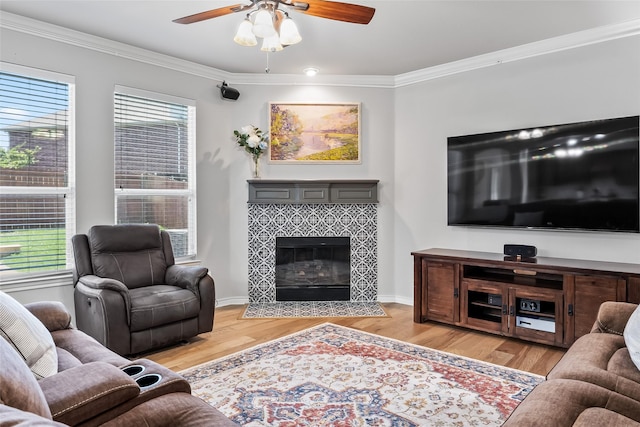 living room featuring crown molding, a ceiling fan, wood finished floors, and a tile fireplace