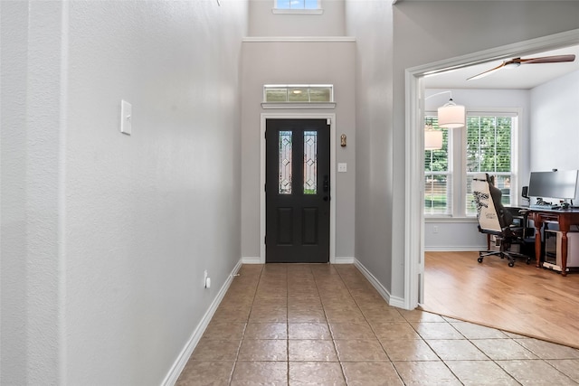 foyer entrance with a healthy amount of sunlight, light tile patterned floors, baseboards, and a ceiling fan