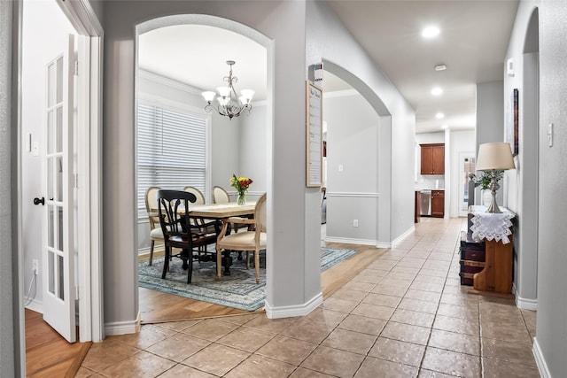 hall featuring baseboards, recessed lighting, arched walkways, light tile patterned floors, and a notable chandelier