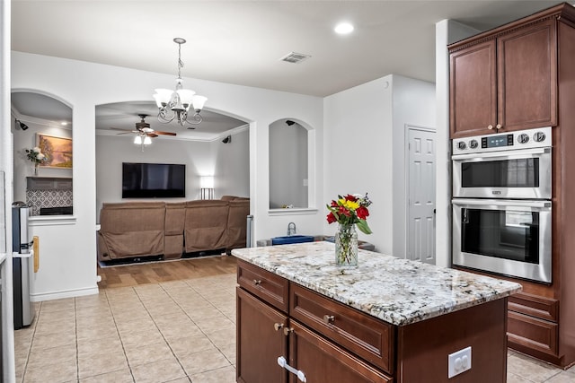 kitchen featuring visible vents, double oven, light stone counters, ceiling fan with notable chandelier, and decorative light fixtures