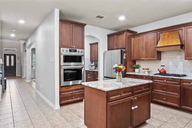 kitchen with appliances with stainless steel finishes, arched walkways, light tile patterned floors, custom range hood, and backsplash