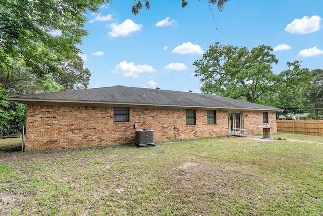 rear view of property featuring a lawn, central AC unit, fence, and brick siding