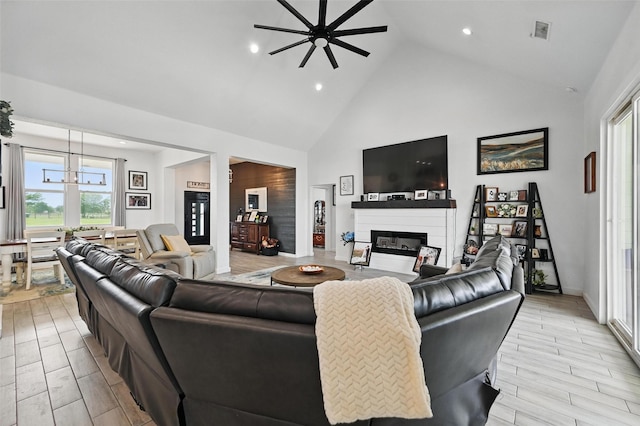 living room with visible vents, a glass covered fireplace, high vaulted ceiling, recessed lighting, and ceiling fan with notable chandelier