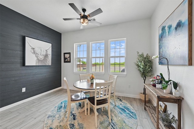 dining space with ceiling fan, light wood-style floors, wood walls, an accent wall, and baseboards
