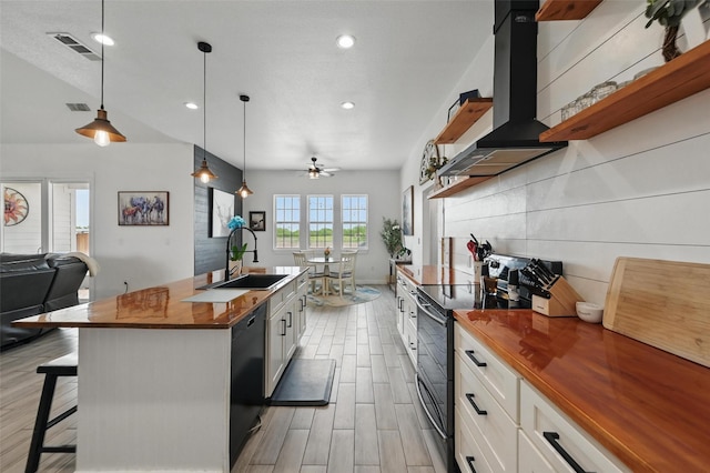 kitchen featuring open shelves, butcher block counters, wall chimney range hood, a sink, and black appliances