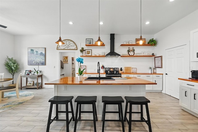 kitchen with open shelves, white cabinetry, a sink, butcher block counters, and wall chimney exhaust hood