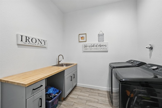 washroom featuring washing machine and dryer, cabinet space, a sink, baseboards, and light wood-style floors