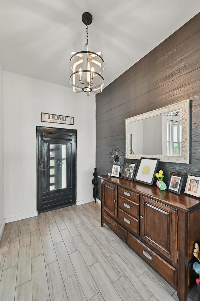 foyer with baseboards, wood walls, a chandelier, and a healthy amount of sunlight
