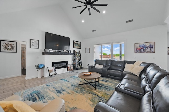 living area featuring visible vents, a glass covered fireplace, wood finished floors, high vaulted ceiling, and a ceiling fan