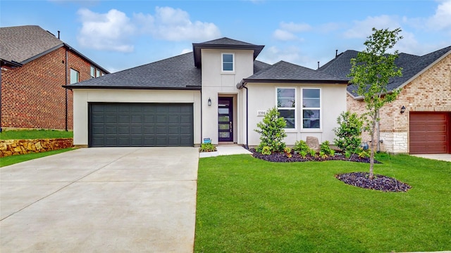 prairie-style home with driveway, a front yard, roof with shingles, a garage, and stucco siding