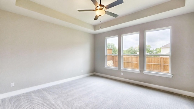 empty room with carpet floors, a ceiling fan, baseboards, and a raised ceiling