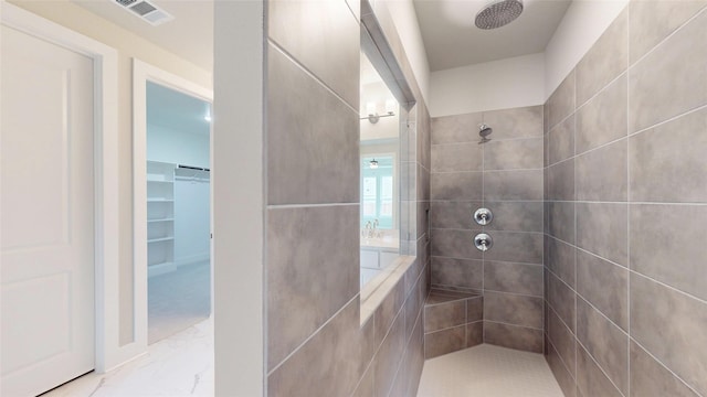 bathroom with visible vents, marble finish floor, a walk in closet, and a tile shower
