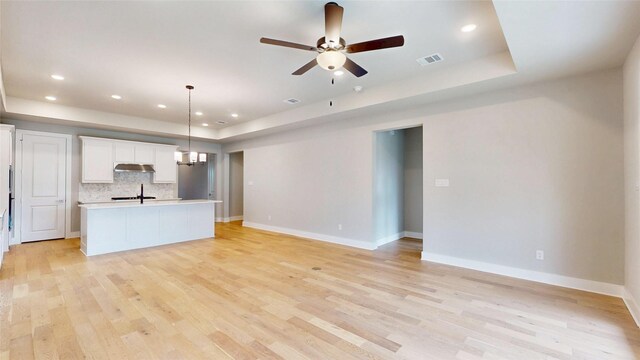 unfurnished living room featuring visible vents, a raised ceiling, and light wood finished floors