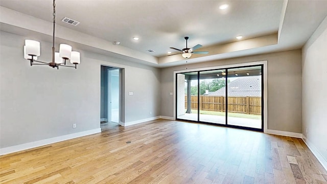 empty room featuring a raised ceiling, light wood-style floors, ceiling fan with notable chandelier, baseboards, and visible vents