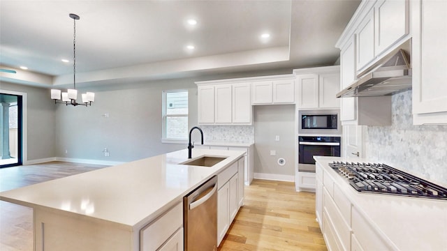 kitchen featuring light wood-style floors, under cabinet range hood, a sink, a notable chandelier, and stainless steel appliances