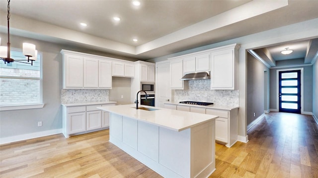 kitchen with a sink, a raised ceiling, stainless steel microwave, and black gas cooktop