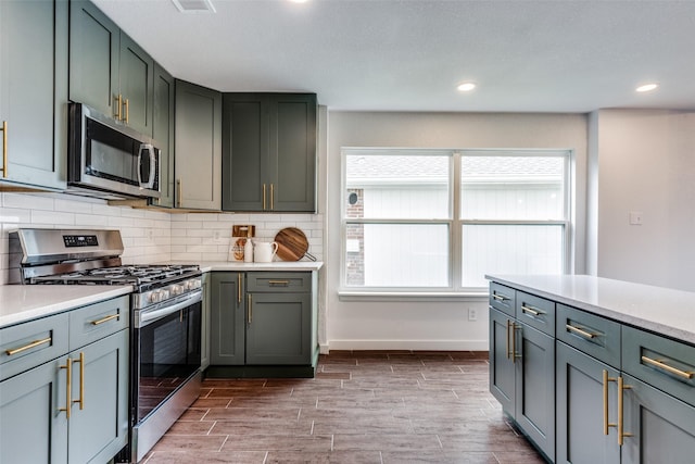 kitchen with decorative backsplash, wood finish floors, light countertops, stainless steel appliances, and recessed lighting