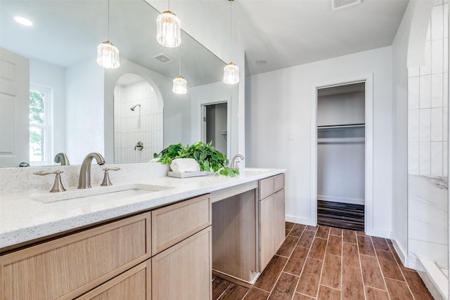 bathroom featuring wood finish floors, a sink, a spacious closet, visible vents, and tiled shower