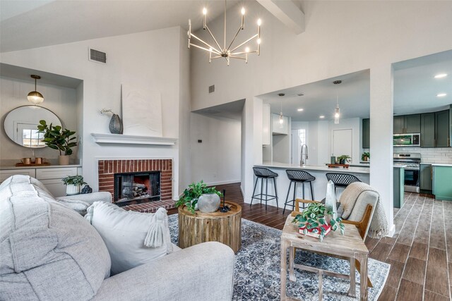 living area with visible vents, a brick fireplace, wood finished floors, high vaulted ceiling, and a chandelier