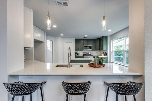 kitchen featuring a sink, stainless steel appliances, a peninsula, tasteful backsplash, and visible vents