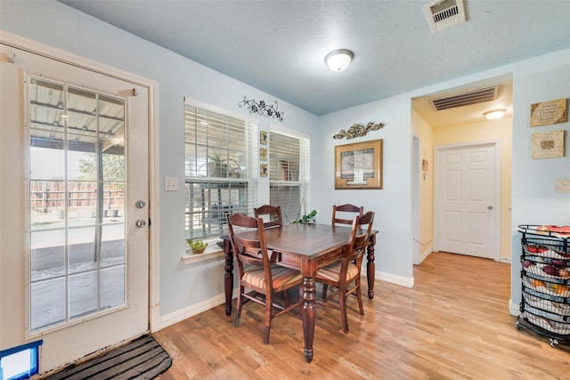 dining space with visible vents, a textured ceiling, light wood finished floors, and baseboards
