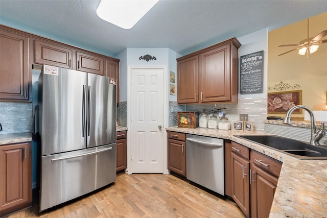 kitchen with a ceiling fan, a sink, light wood-style flooring, backsplash, and stainless steel appliances