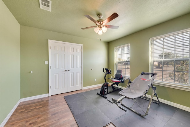 exercise area with ceiling fan, a textured ceiling, baseboards, wood finished floors, and visible vents