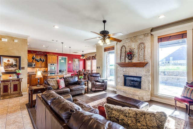 living room featuring ornamental molding, a stone fireplace, baseboards, recessed lighting, and a ceiling fan