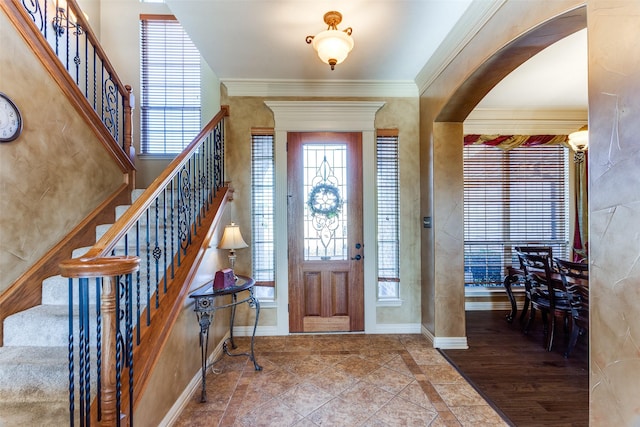 foyer entrance featuring baseboards, arched walkways, stairs, and a wealth of natural light