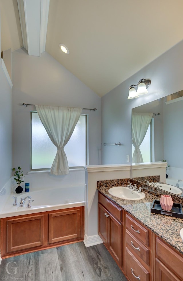 bathroom featuring vanity, a garden tub, wood finished floors, and lofted ceiling