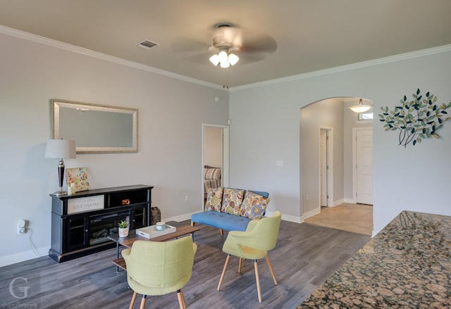living room with a ceiling fan, visible vents, arched walkways, wood finished floors, and ornamental molding