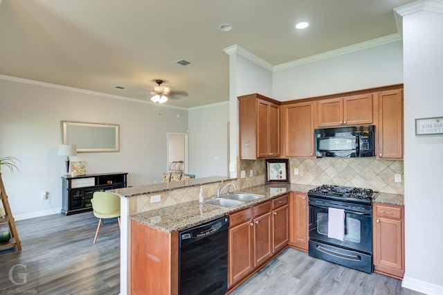 kitchen with backsplash, a sink, black appliances, a peninsula, and light wood-style flooring
