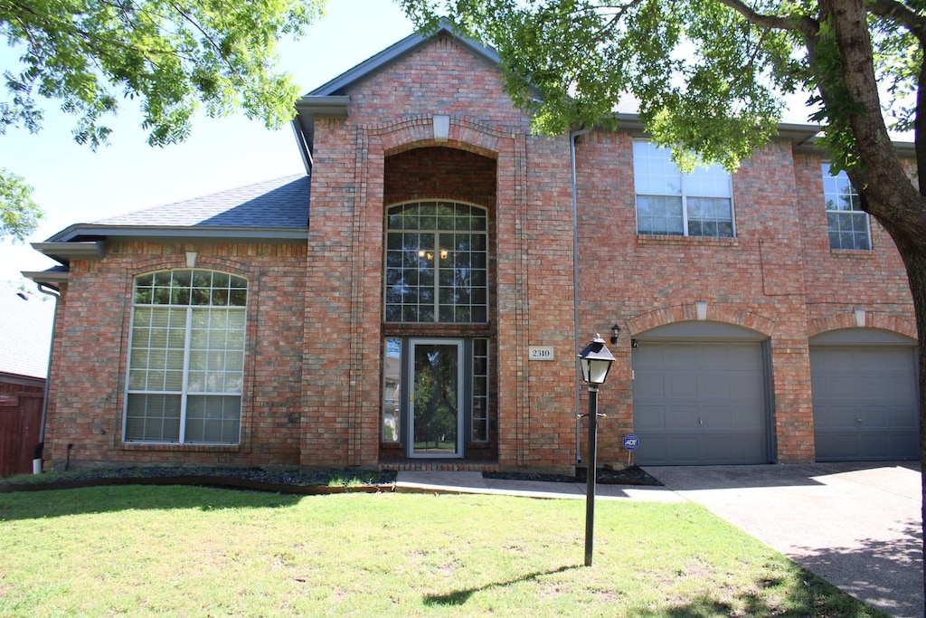 traditional-style home featuring driveway, roof with shingles, brick siding, a front lawn, and an attached garage