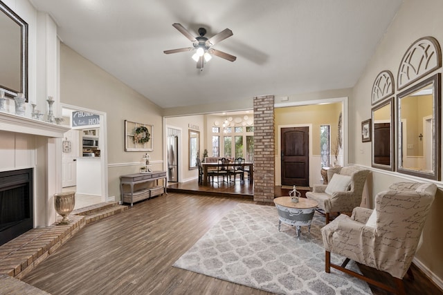 living area with a ceiling fan, a fireplace with raised hearth, wood finished floors, and lofted ceiling