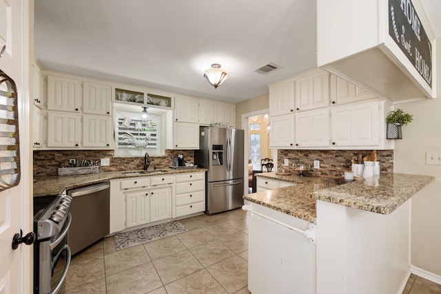 kitchen featuring stainless steel appliances, decorative backsplash, a sink, and a peninsula