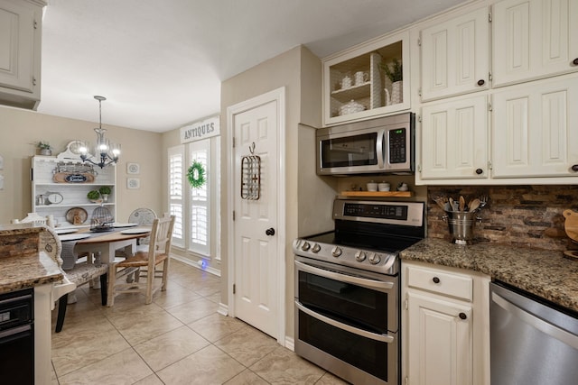 kitchen with an inviting chandelier, decorative backsplash, glass insert cabinets, appliances with stainless steel finishes, and decorative light fixtures