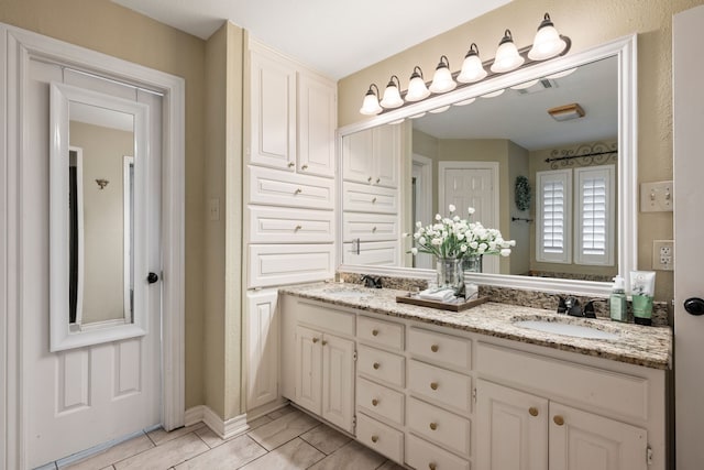 full bath featuring double vanity, a sink, baseboards, and visible vents