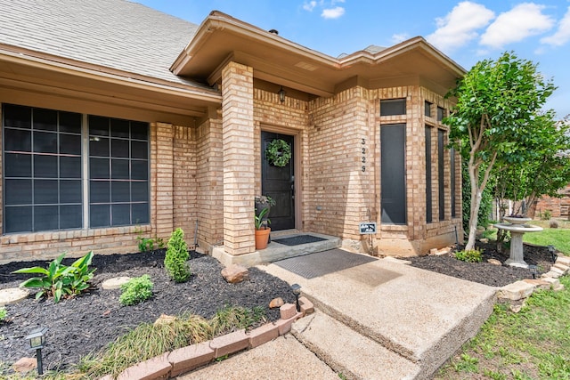 entrance to property featuring brick siding and a shingled roof