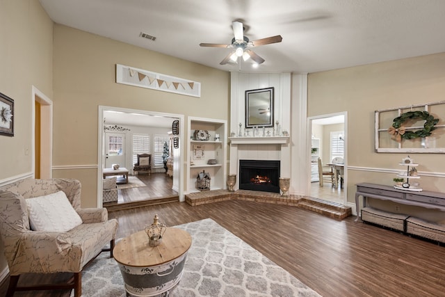living room featuring a brick fireplace, a ceiling fan, wood finished floors, a towering ceiling, and visible vents