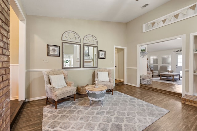 living area with visible vents, baseboards, a towering ceiling, and wood finished floors