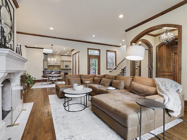living room featuring arched walkways, stairs, a notable chandelier, and ornamental molding