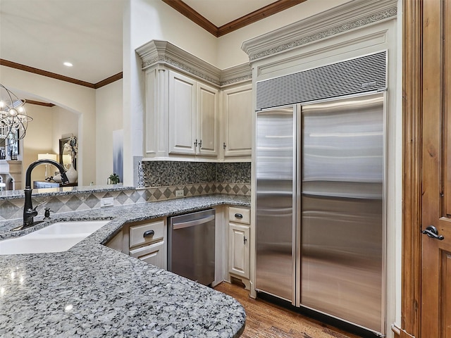 kitchen featuring backsplash, crown molding, appliances with stainless steel finishes, a sink, and light stone counters