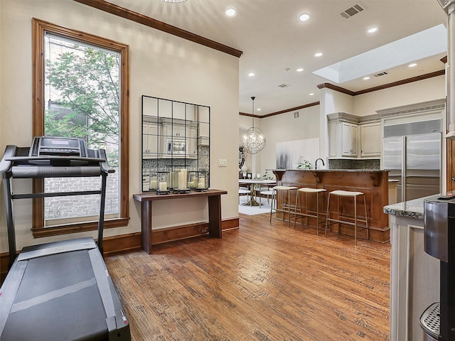 kitchen with crown molding, a breakfast bar, wood finished floors, built in refrigerator, and visible vents