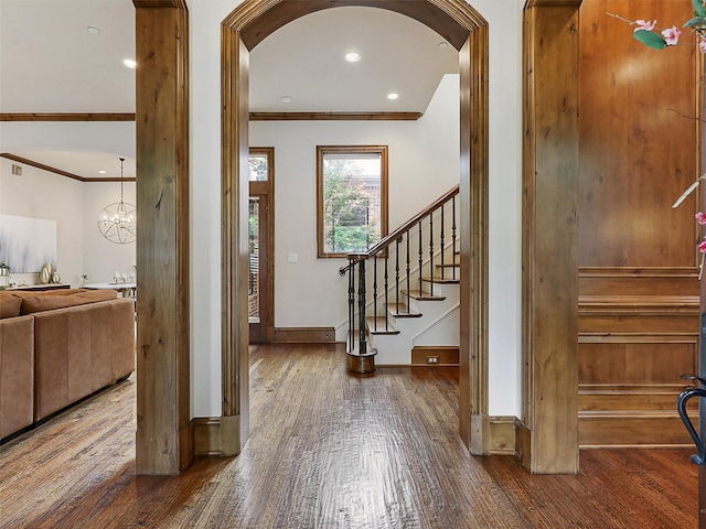 foyer with crown molding, arched walkways, stairway, and wood finished floors