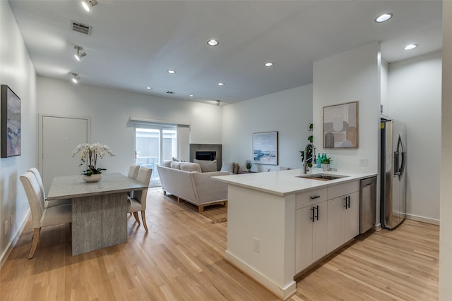 kitchen featuring a sink, a tiled fireplace, stainless steel appliances, light wood-type flooring, and visible vents